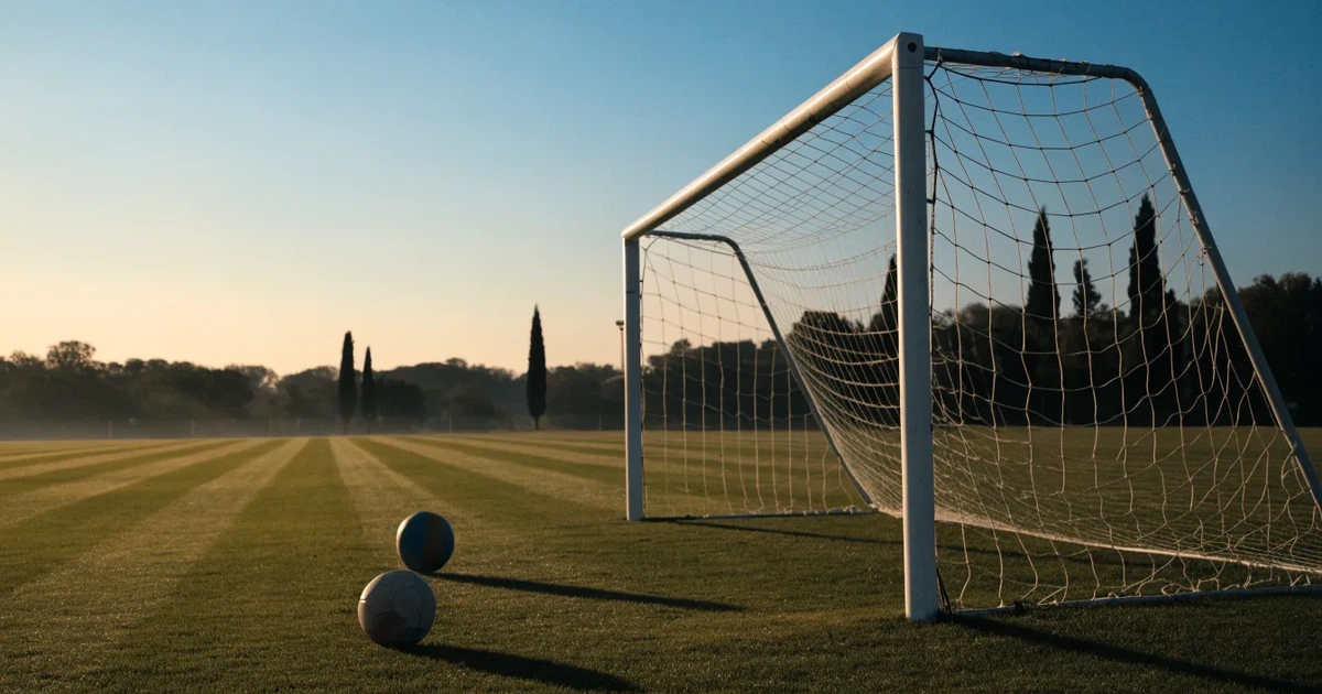 Ein Fußballtor mit Netz auf einem leeren Platz im Abendlicht, der Rasen frisch gemäht, im Hintergrund Zypressen.