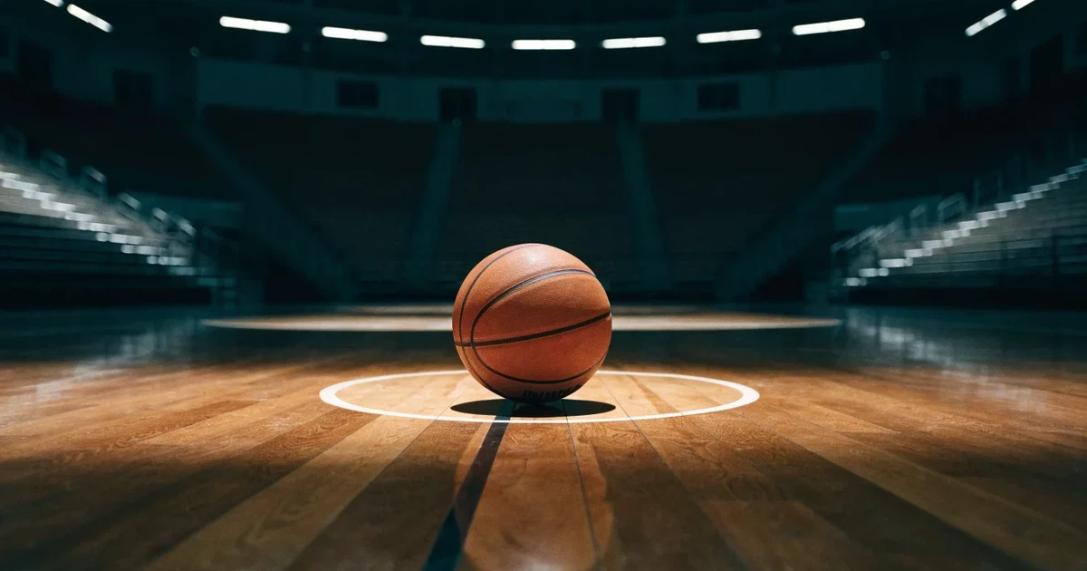 Ein Basketball liegt auf dem Parkettboden einer leeren Arena, Scheinwerfer werfen Licht auf die Mittellinie.